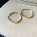 Nahaufnahme minimalistischer vergoldeter glatter runder Creolen auf einer Textur - Glatter Runder Creolen-Stil / Gold