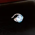 Detailansicht eines ovalen hellblauen Zirkon-Ohrclips mit hohlem silbernen Metalldesign. - Ohrclips / Einzelstück / Silber-Blau