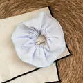 Gedetailleerd overzicht van lichtblauwe scrunchie van getextureerde stof op een rietmat - Blauwe Gestructureerde Stof Stijl
