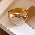 Macro view of gold-tone pleated cuff bracelet with large oval white resin inlay - Gold-White