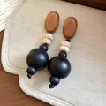 Nahaufnahme von eleganten handgefertigten Holz- und Acrylperlen-Ohrringen auf beigem Stoff - Silbernadel - Kaffee - Schwarz