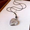 Detail shot of a silver heart pendant necklace with floral engraving and black cord. - Heart Engraved Pendant (HN13531) / Silver Heart + Black Leather Rope