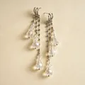Détail rapproché de boucles d'oreilles à pompons argentés avec gouttes en verre clair - Blanc