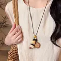 Detailed view of a retro ethnic style wooden cat pendant necklace with leather cord on model - Coffee-White Cat