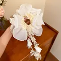 Close-up detail showing the elegant texture of a cream organza scrunchie with floral tassels - Beige