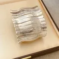Gros plan d'un bracelet manchette métallique à texture ondulée dans un coffret à bijoux - Style Plissé Ondulé / Argent