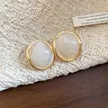 Close-up of vintage oval resin stud earrings with gold-tone frames on woven fabric. - White