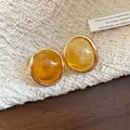 Close-up of retro oval resin earrings with a translucent amber finish and gold-tone frame. - Amber