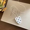 Détail d'un collier porte-lunettes vintage à pois blancs et noirs posé sur un livre ancien. - Blanc