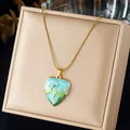 Gros plan d'un pendentif cœur en émail bleu avec motif floral peint sur chaîne dorée - Style de Cœur Peint à l'Émail (N4588)