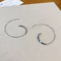 Nahaufnahme von minimalistischen silbernen C-förmigen Spiralohrringen auf Papier - Haken-Stil / Silber