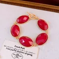 Macro-opname van rode ovale harsstenen op een gouden armband met toggle-sluiting - Rood