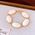 Gedetailleerd overzicht van gefacetteerde witte hars ovalen op gouden armband - Wit