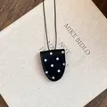 Detailansicht einer schwarzen Leder-Brillenclip-Halskette mit Punkten auf Buch. - Schwarz