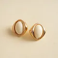 Makro-Detail von Retro-Ohrsteckern mit cremefarbenem Acryl-Oval und Gold-Finish - Beige