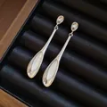 Elegante silberne Hängeohrringe mit weißen Katzenaugenstein-Anhängern auf Samt - Silbernadel-Anhänger-Stil / Silber