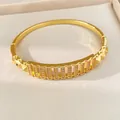 Nahaufnahme eines vergoldeten Armreifs mit Zirkonia-Pflaster und geometrischen Nieten. - Gold