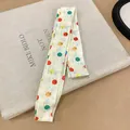 Detail of a white skinny scarf with colorful polka dots on a minimalist book background. - Yellow