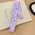 Detailed view of a purple polyester twilly scarf with colorful polka dots on a book - Purple