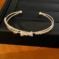 Detailansicht eines doppellagigen goldenen Armreifs mit funkelndem Zirkonia-Schleifen-Design. - Gold