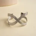 Vue macro montrant la texture plissée et le design croisé multicouche du bracelet argenté. - Argent