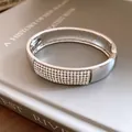 Detailed close-up of a silver pavé crystal oval bangle on a grey book background. - Rhinestone Hollow Oval Bracelet