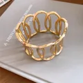 Detailed macro view of a gold-tone metal open cuff bracelet with oval cut-out design. - Hollow Oval Geometric Bracelet