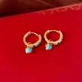 Détail de boucles d'oreilles créoles dorées avec coeurs bleus sur un coffret à bijoux rouge - Créoles - Cœur Bleu (Style Or)