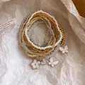 Detailansicht eines böhmischen Perlenarmband-Sets mit weißen Blumen- und Schmetterlingsanhängern - 9-teiliges Set / Gold-Weiß-Kaffee-Transparent
