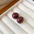 Nahaufnahme minimalistischer dunkelroter Tropfenohrstecker in einer cremefarbenen Schmuckdose - Dunkelrot