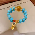Macro view of a turquoise-style beaded bracelet with golden gourd and lotus charms - Gold-Blue-Yellow