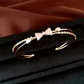 Detailansicht eines goldenen zweilagigen Armreifs mit funkelndem Zirkon-Schleifenmotiv. - Gold