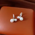 Nahaufnahme von silbernen Creolen mit asymmetrischen weißen Doppelperlen auf orangefarbenem Leder. - Doppelperlen-Creolen-Ohrringverschluss (22#) / Silber