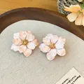 Detailopname van roze bloem oorknopjes met gouden hart op een beige stoffen ondergrond. - Roze