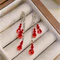 Detail view of elegant silver tassel earrings with vibrant red faceted teardrop beads. - Red