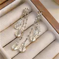 Close-up detail of silver needle multi-layer tassel earrings with clear faceted crystal drops. - White