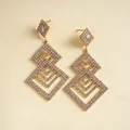 Nahaufnahme eleganter goldfarbener Ohrringe mit geometrischen Rautenformen und Strasssteinen. - Gold