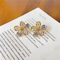 Détail de boucles d'oreilles fleurs dorées avec cristaux bleus et perles sur un livre. - Motif floral / Tige en argent 925 / Or