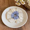 Vue détaillée d'un chouchou en satin crème et tissu rayé bleu posé sur une assiette blanche. - Chouchou Plissé Patchwork Satin / Style Contrasté Blanc et Bleu