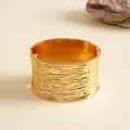 Detailweergave van een brede gouden armband met een elegante gerimpelde golftextuur. - Breed Model / Goud
