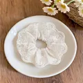 Détail d'un chouchou en dentelle blanche avec broderie florale posé sur une assiette blanche - Chouchou Floral Brodé / Style de Dentelle Blanche