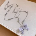 Elegante lange Perlenkette mit einem weißen gepunkteten Schleifenanhänger auf einem Buch - Weißes Punktmuster-Schleifen-Stil