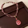 Détail d'un collier bohème avec pendentif goutte en strass rouges sur plateau brun - Pendentif Forme de Poire / Rose rouge