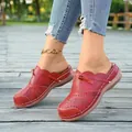 Detail shot of red leather mules featuring laser-cut patterns and decorative ties on a boardwalk. - 36 / Red