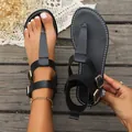 Close-up detail of black T-strap flat sandals with gold buckles shown on wooden floor - 36 / Black