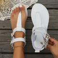 Close-up of stylish white T-strap flat sandals with gold buckles on wooden background. - 36 / White