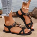 Detailansicht schwarzer flacher T-Riemen-Sandalen mit Boho-Blumenschmuck auf Strandsand. - 36 / Schwarz