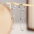 Macro view of minimalist stainless steel chain tassel earrings on a display stand. - Silver