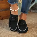 Close-up of elegant black suede flat mules with white contrast stitching worn on foot - 36 / Black