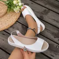 Close-up view of white peep-toe flat sandals with elastic straps on a wooden floor - 36 / White